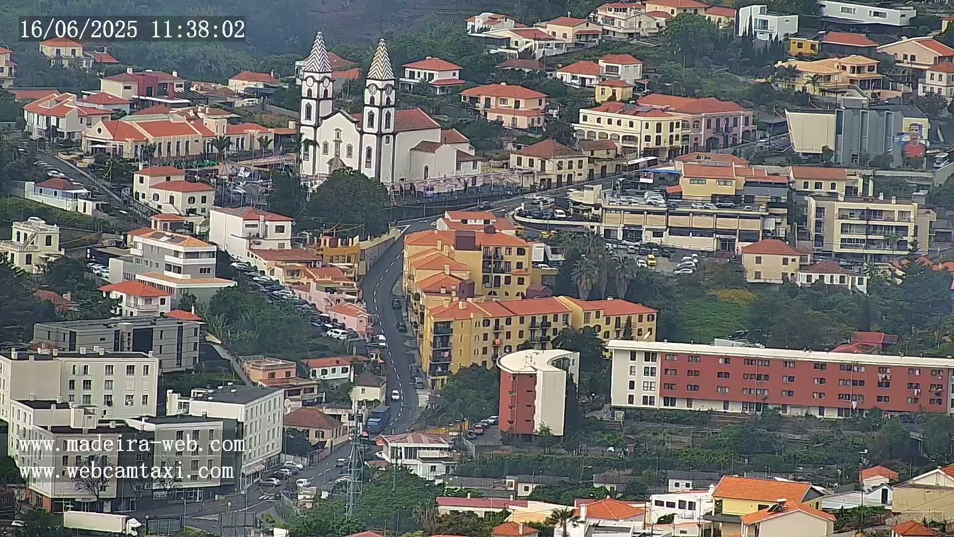 An aerial view of a town with red-tiled roofs, a prominent white church, and overcast weather conditions.