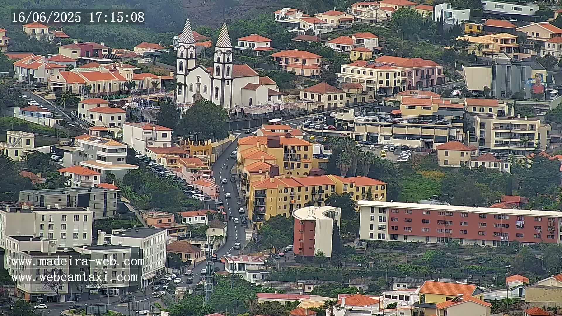 A high-angle view of a densely populated area with predominantly red-roofed buildings, a prominent white church, and overcast weather conditions.