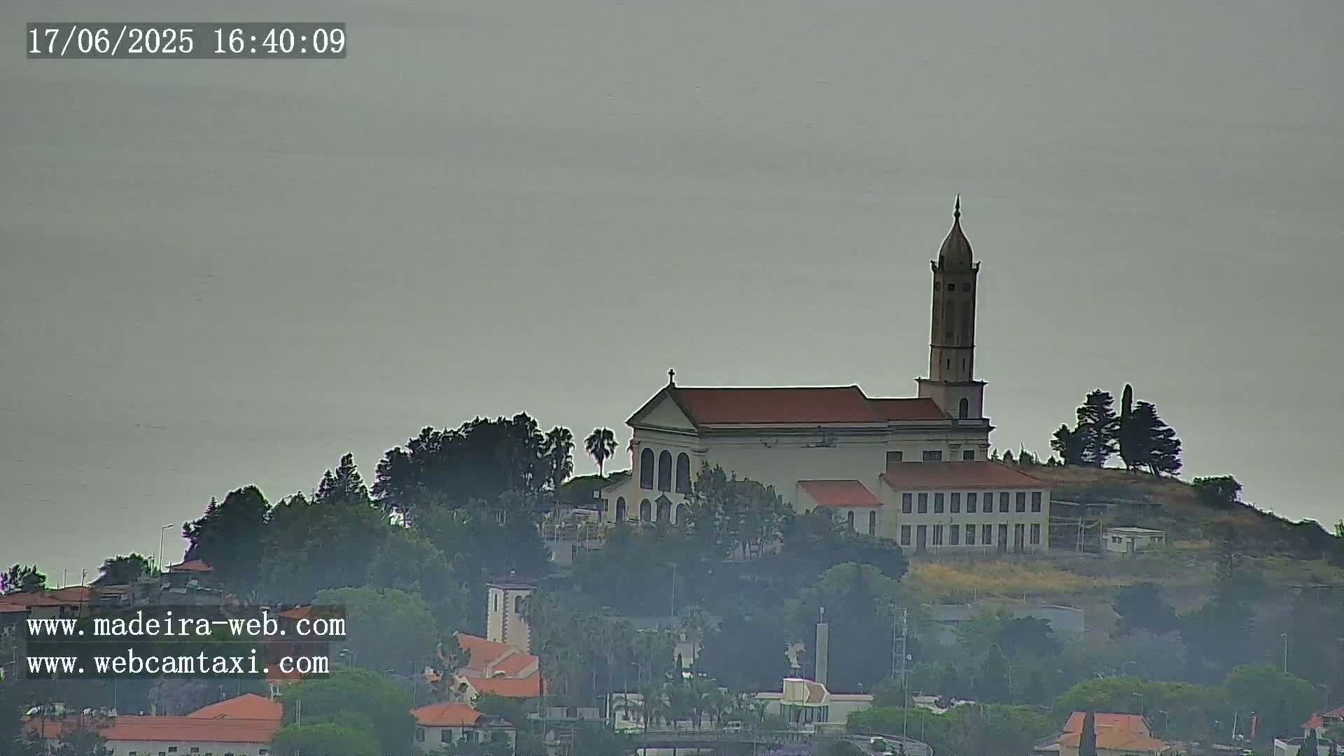 A church with a tall tower sits atop a hill shrouded in hazy weather, overlooking a town below.