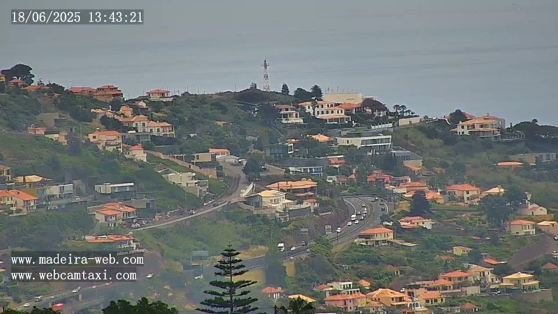 A hillside covered in houses and vegetation overlooks a highway with light traffic, all under an overcast sky.