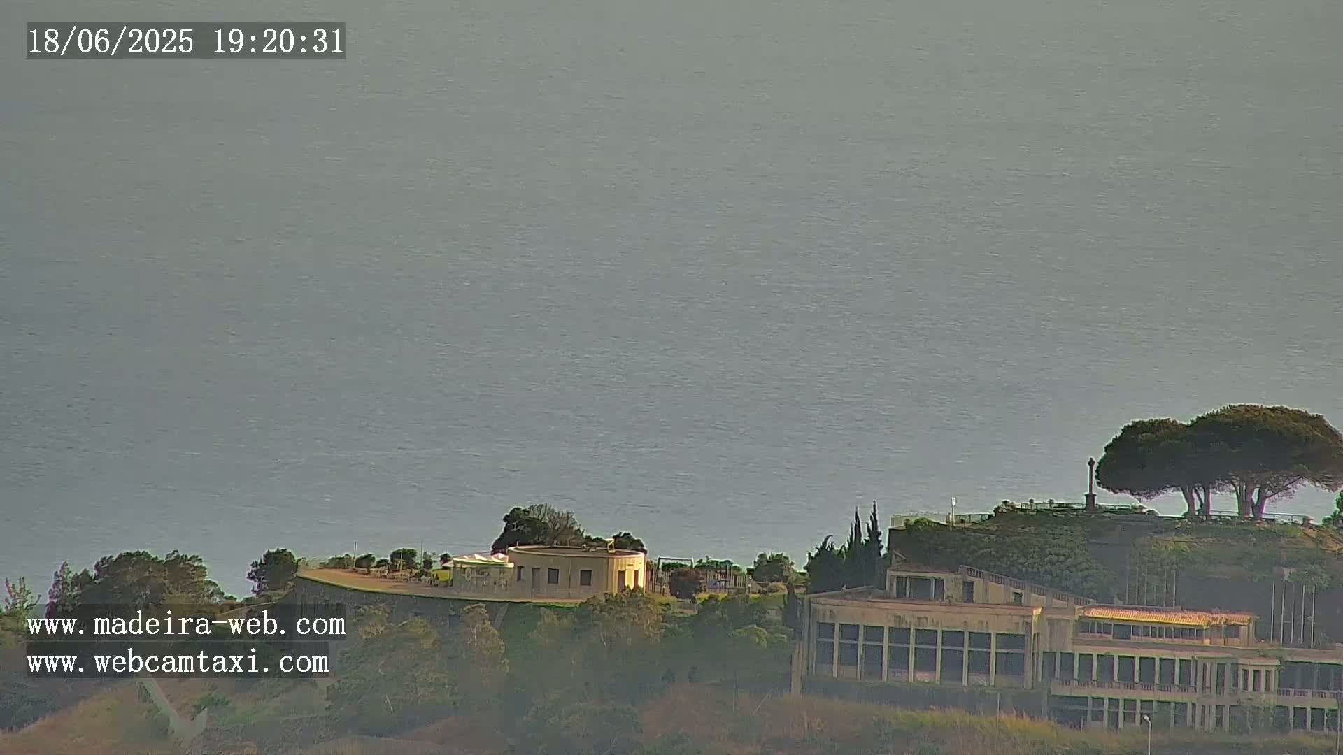 A calm, gray ocean is visible in the background, with buildings and trees situated on a hill overlooking it.