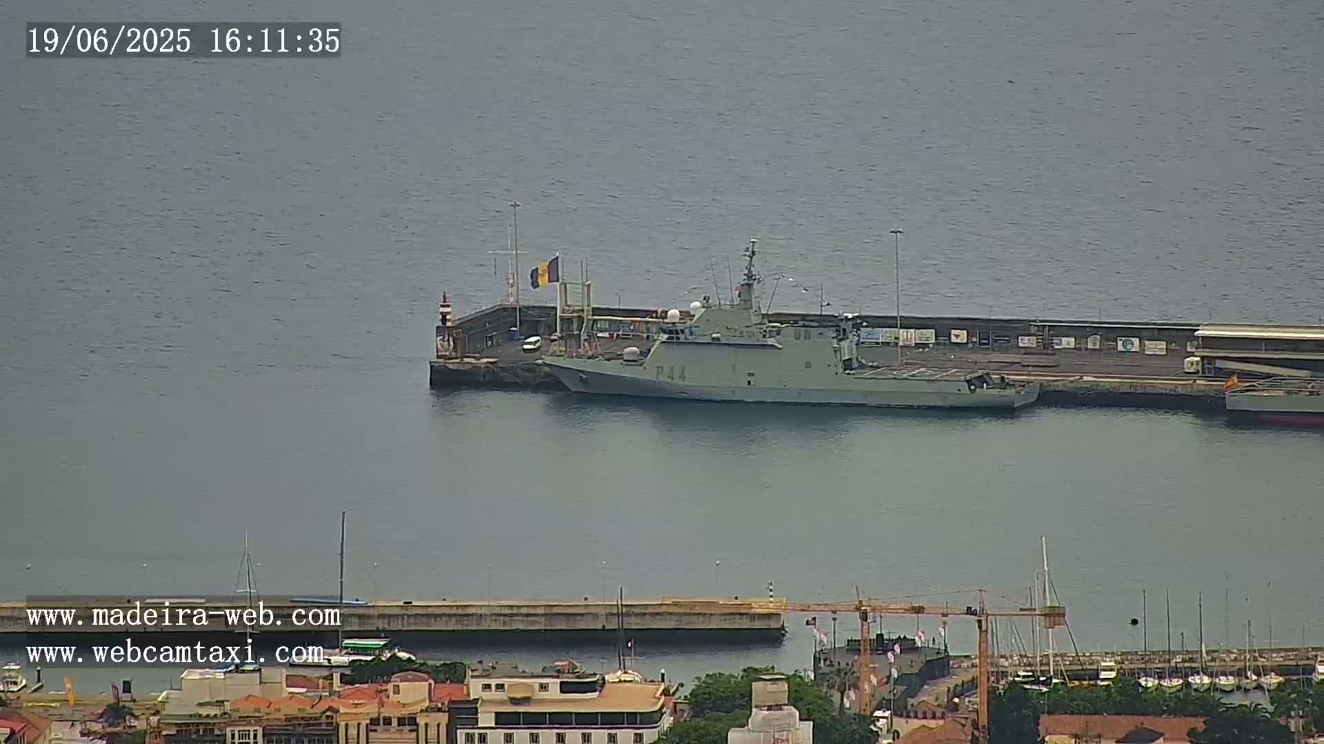 A military ship is docked at a harbor on a calm, overcast day.