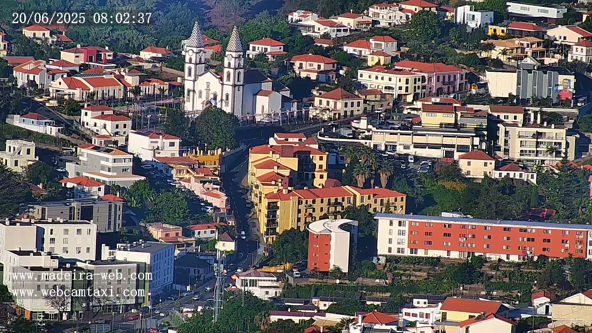 An aerial view of a town on a sunny day, showing a variety of buildings including a prominent church, apartments, and houses.
