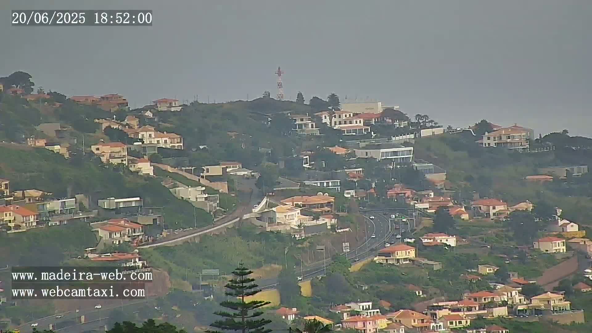 A hazy view of a hillside covered in houses and a highway, with a communications tower visible in the distance.