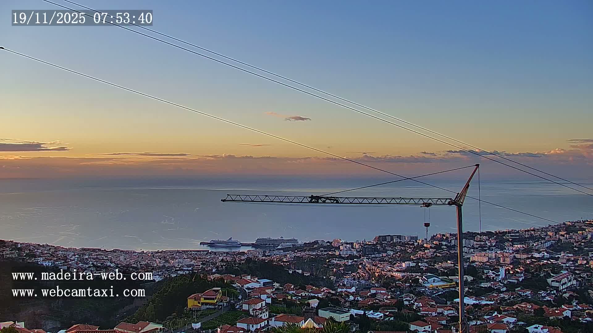 A hazy, overcast sky overlooks a hillside with several buildings, including a large, long structure, and some trees.
