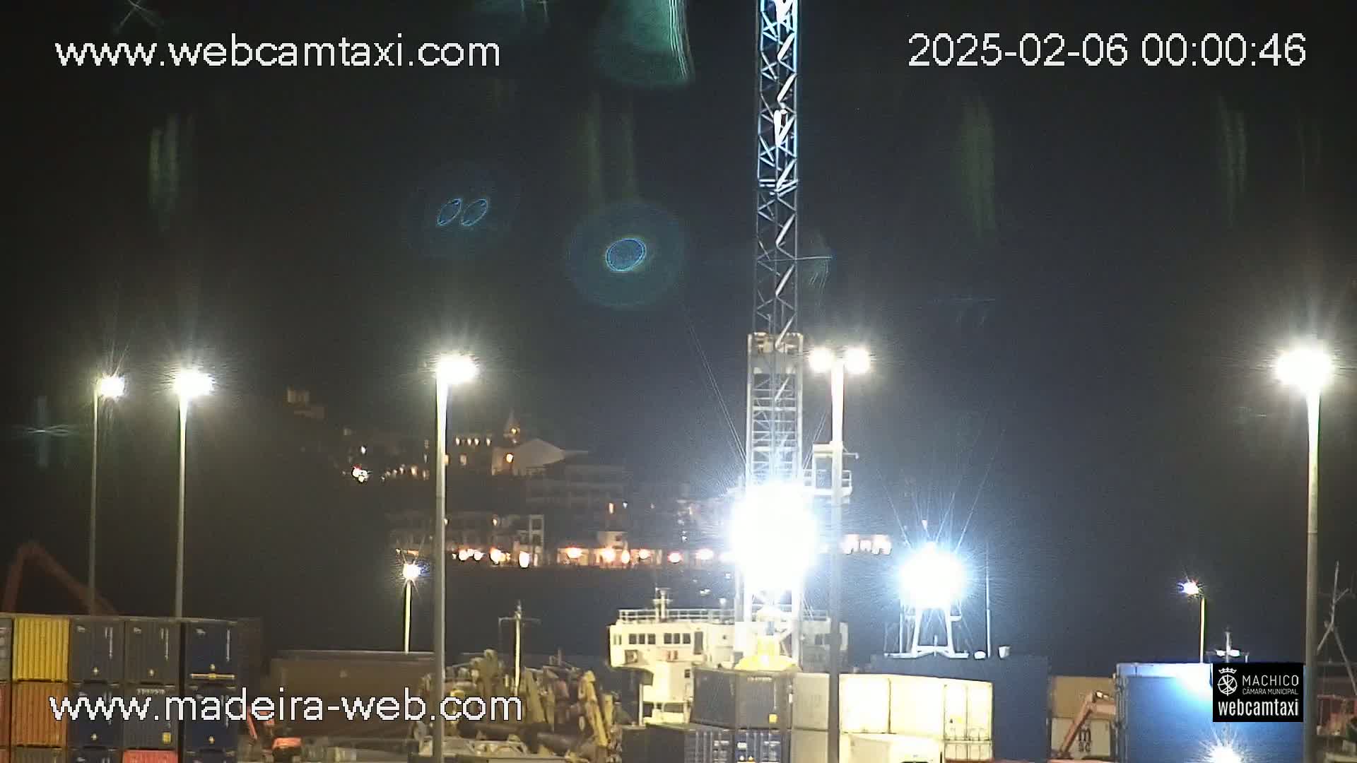 At night, brightly lit cargo containers and a large ship are visible near a tall crane under a clear, dark sky.