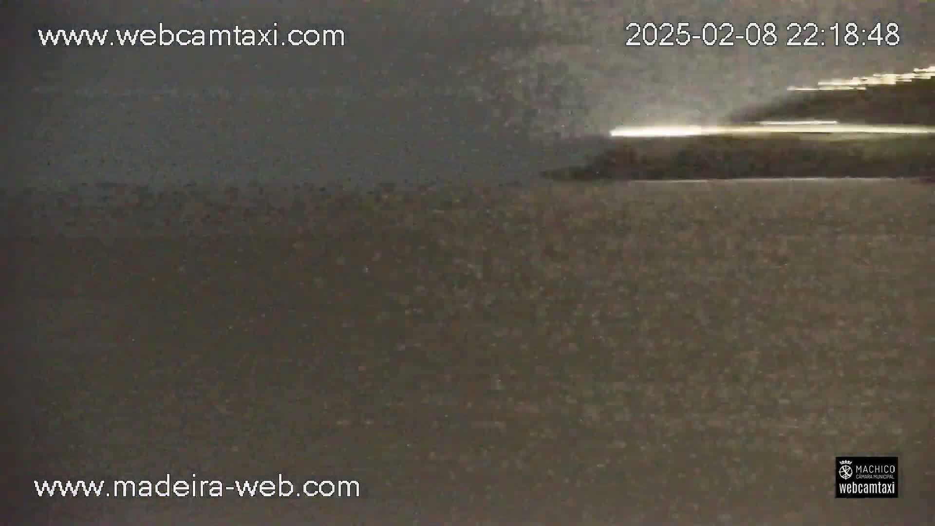 A dark, possibly nighttime, outdoor scene shows a dimly lit body of water with a faint light source in the distance.