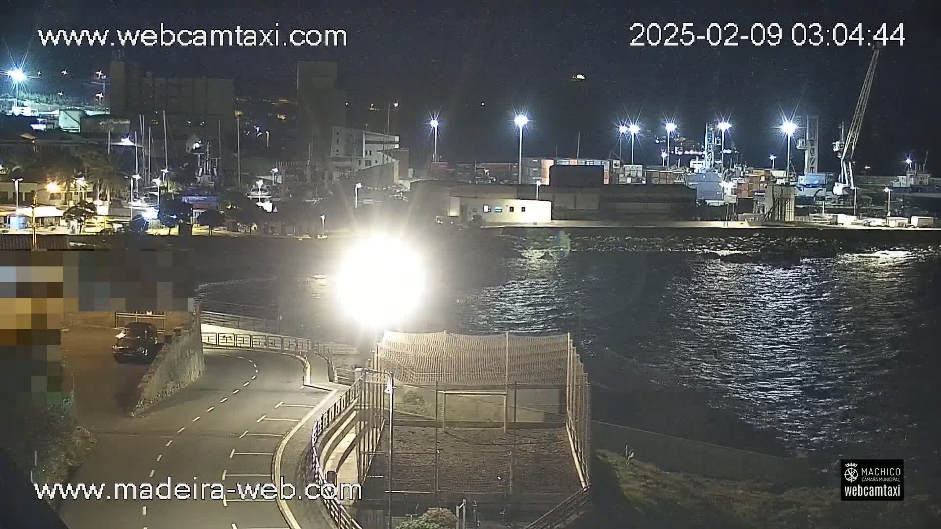 A nighttime view of a harbor with boats and buildings, and a calm body of water.