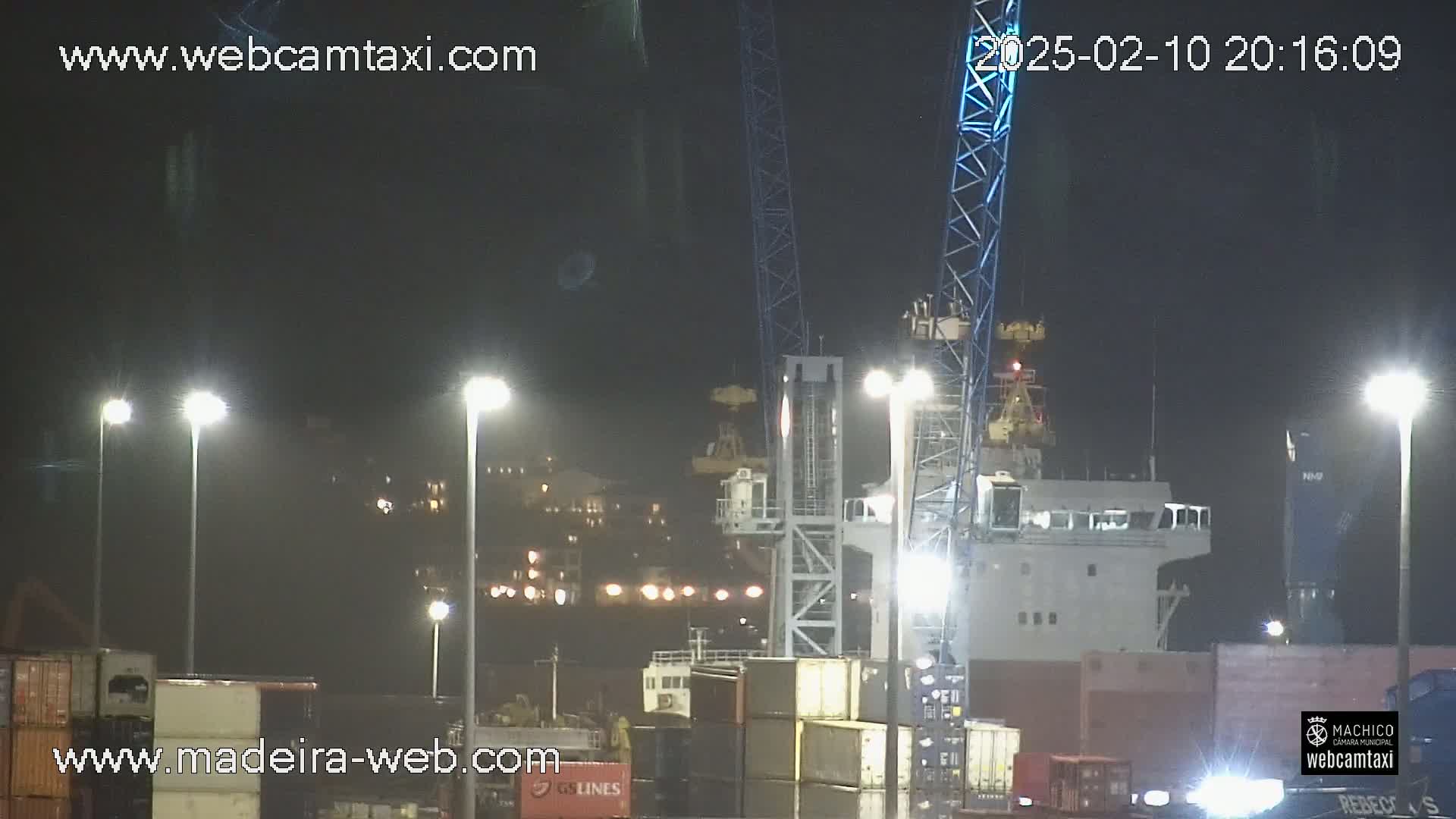 A nighttime view of a port with a large ship and several cranes under bright lights.