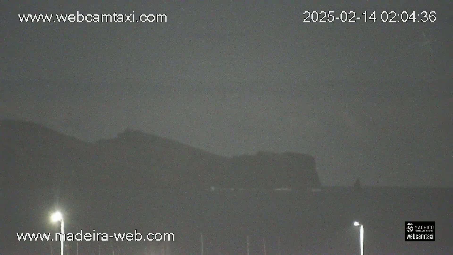 A nighttime, overcast view shows dark hills in the distance, illuminated by two streetlights in the foreground.
