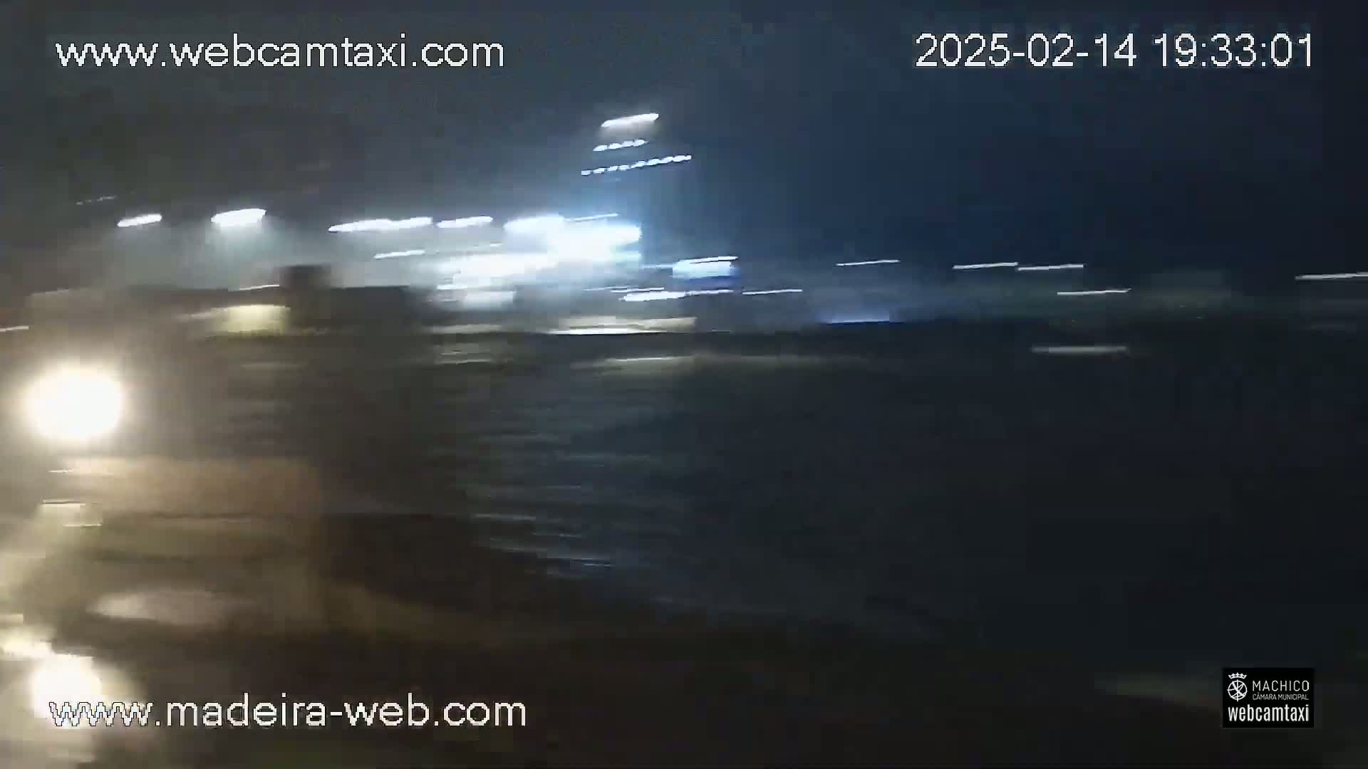 A nighttime view of blurred headlights and lights from buildings in rainy conditions.