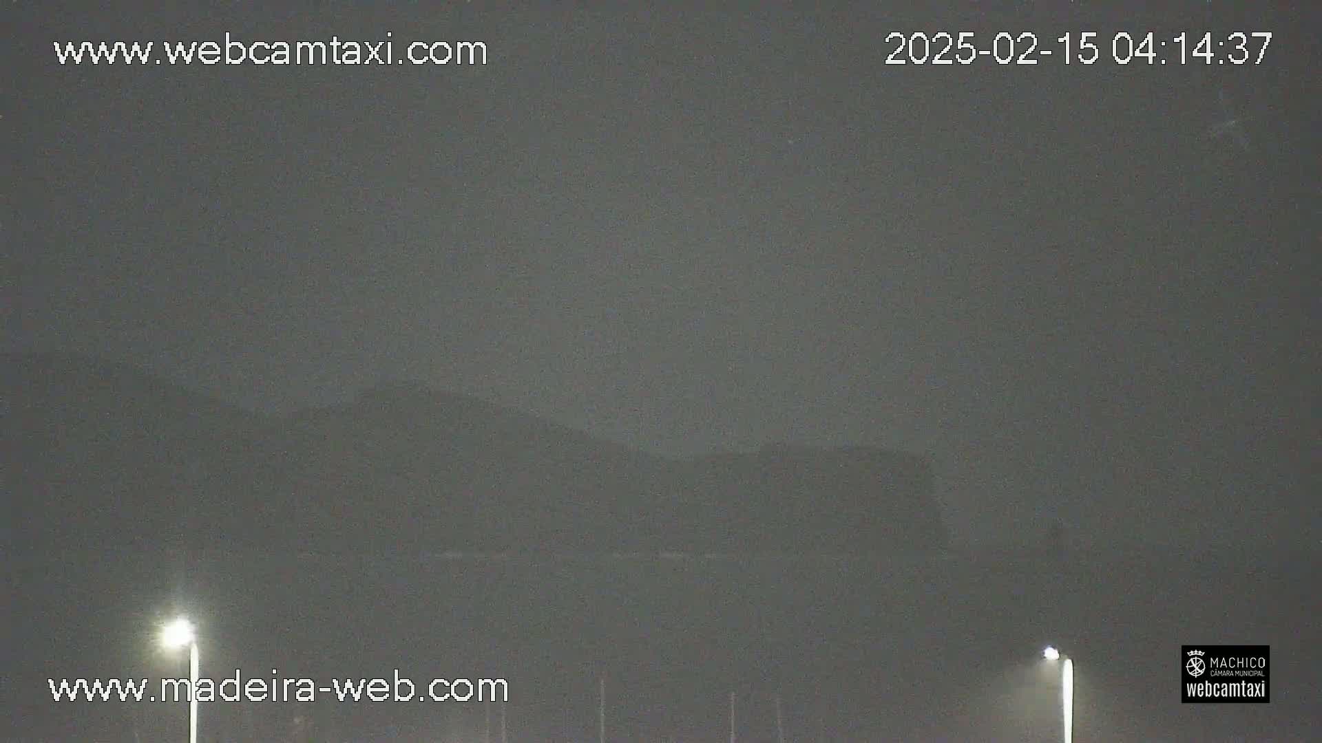 A hazy, dark nighttime scene shows dimly lit streetlights and dark mountains in the distance.