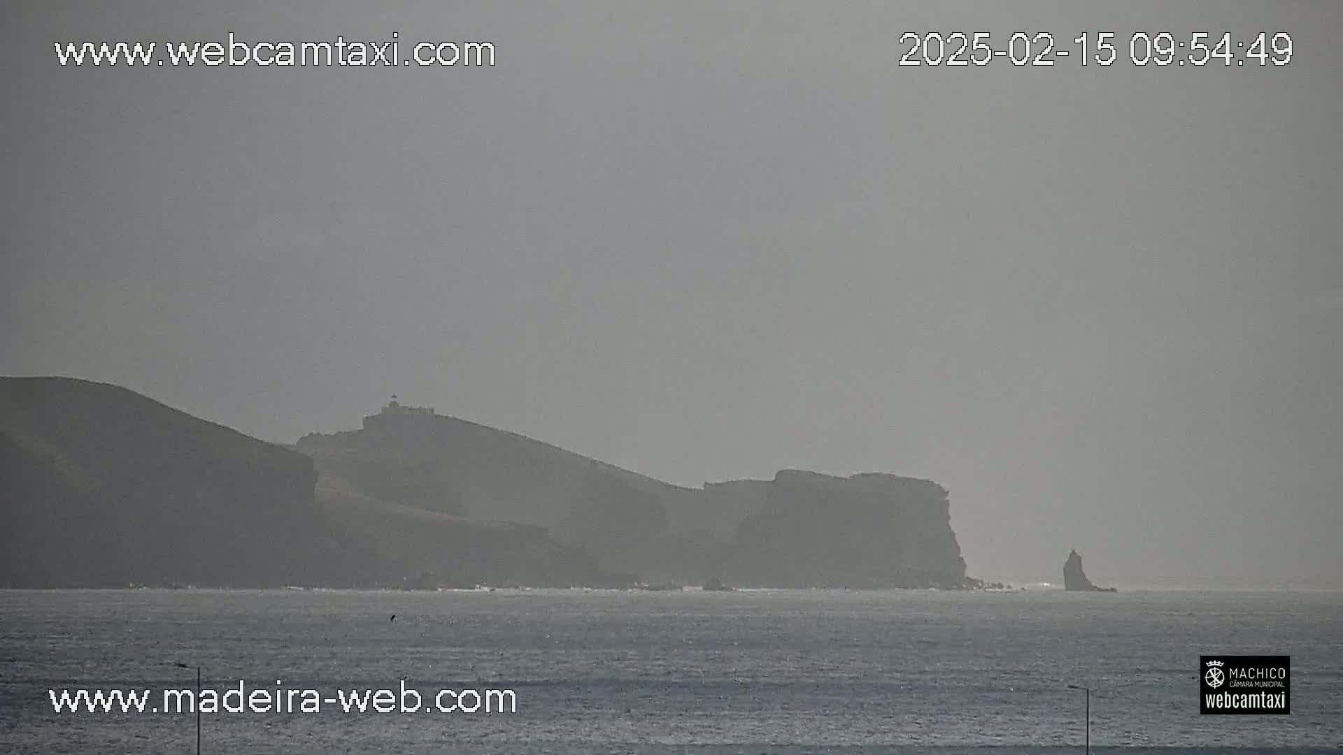 A hazy view of dark, rocky cliffs and a small island jutting out into a calm sea.