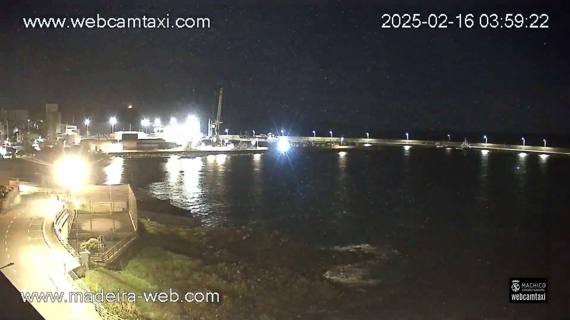 A nighttime view of a harbor with a pier, calm water, and a few lights illuminating the scene.