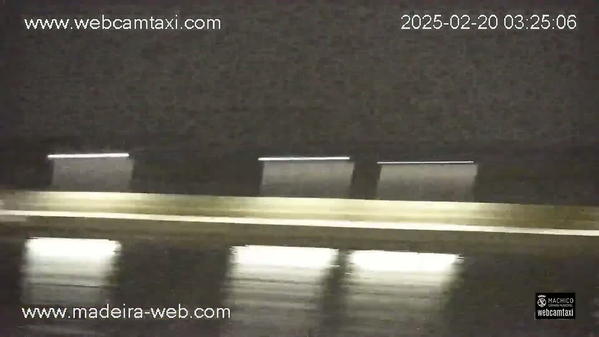 A nighttime view of a wet road inside a tunnel, illuminated by several overhead lights.
