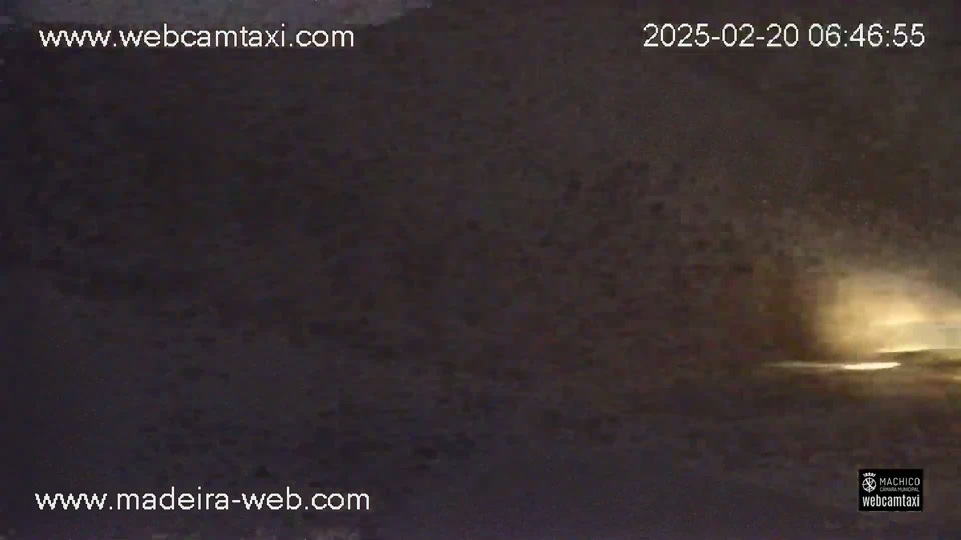 A nighttime, low-light outdoor scene shows a dark, possibly cloudy sky with a faint, bright glow on the horizon.