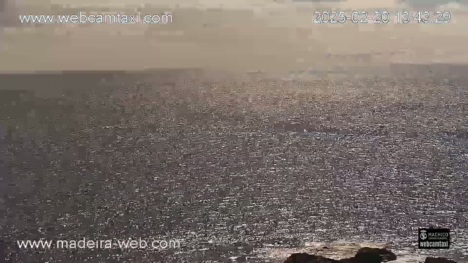 A hazy, sunny day shows a vast expanse of sparkling ocean meeting a rocky shoreline.