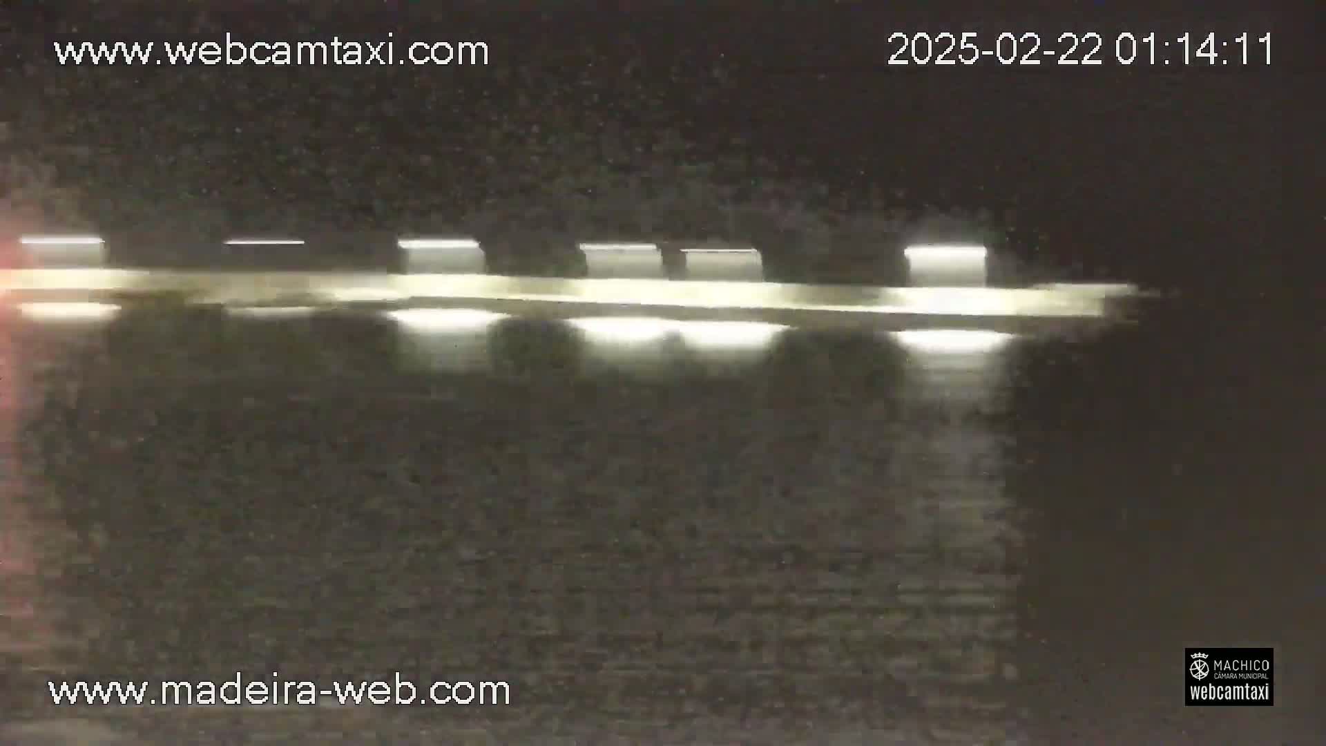A nighttime view of a long, low structure with regularly spaced lights reflecting on dark water.