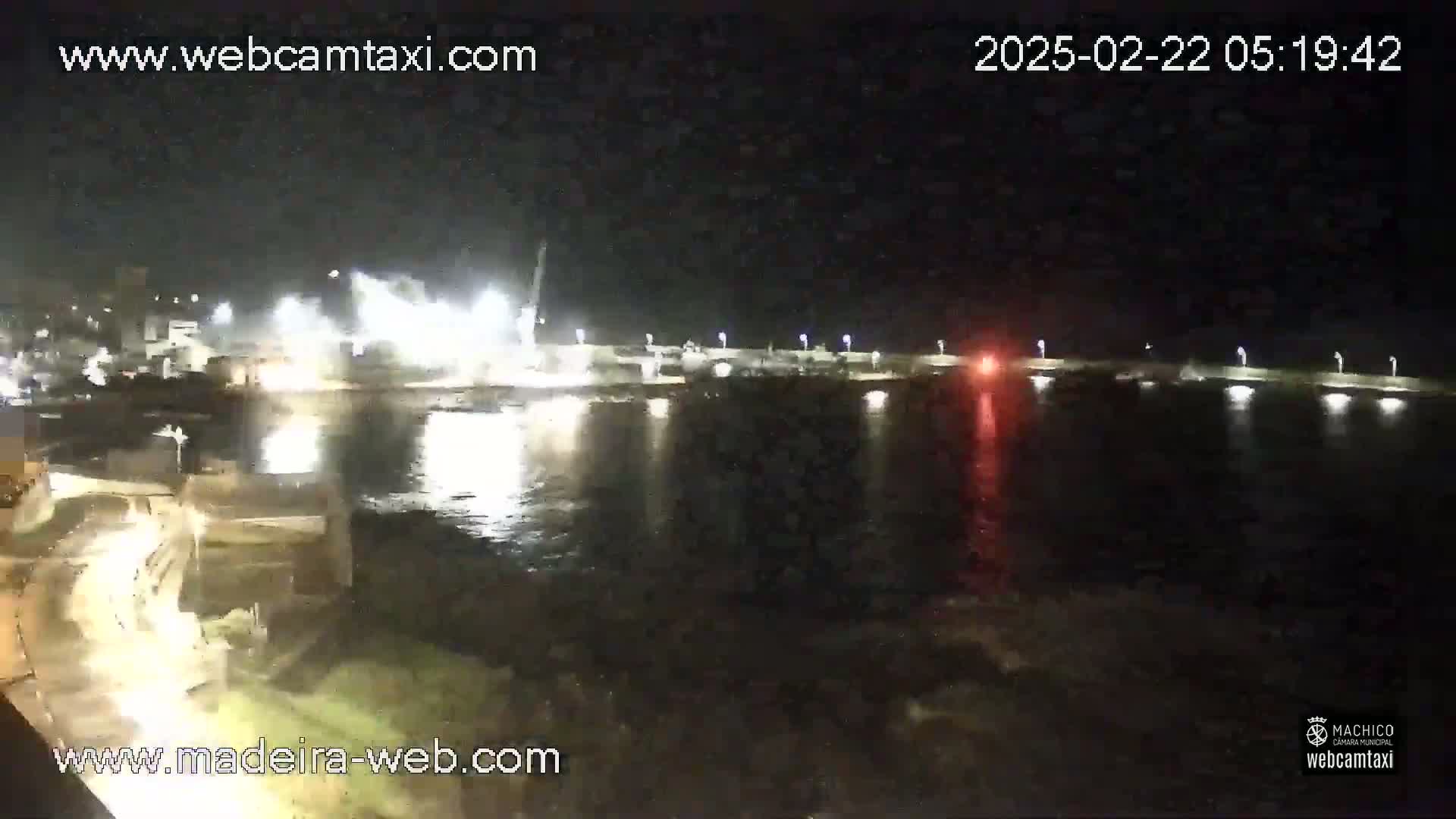 A nighttime view of a body of water with bright lights reflecting on the surface near a structure, showing some construction activity.