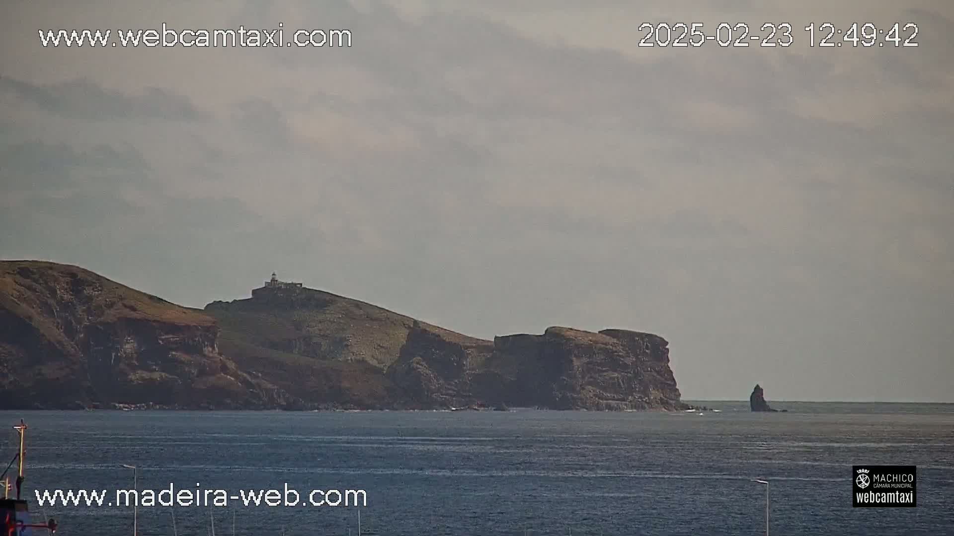 A rocky island with a lighthouse, partially obscured by overcast skies, is visible across a calm body of water.