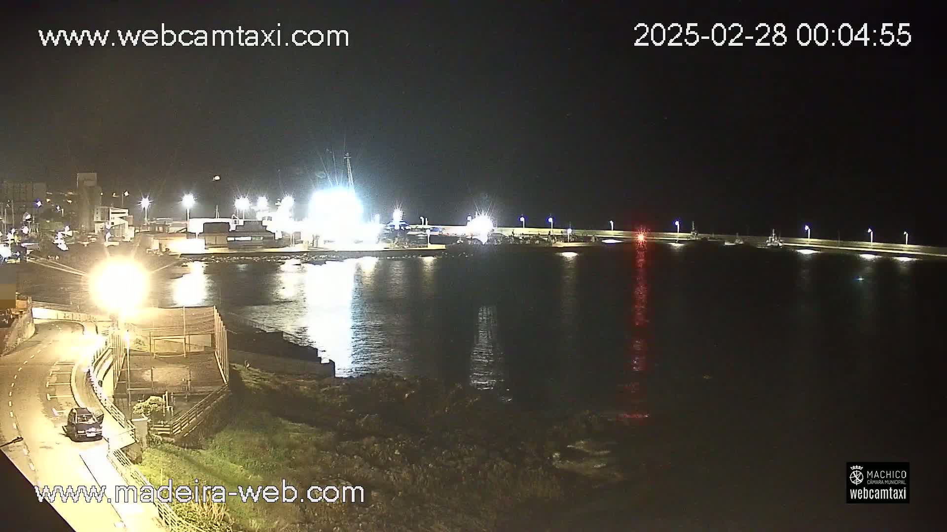 A nighttime view of a harbor with calm water reflecting the lights from buildings and boats on the docks.