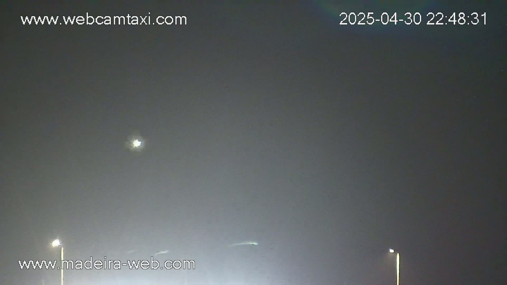 A night scene shows a mostly cloudy sky with two distant lights on poles and a bright light possibly from the moon or a planet.