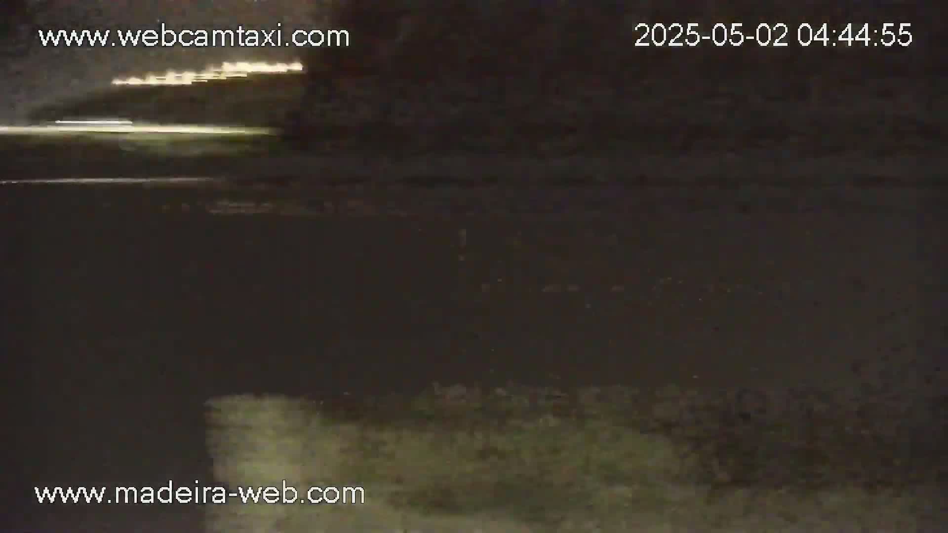A nighttime, low-light view of a dark body of water, possibly the ocean, with faint lights visible in the distance.