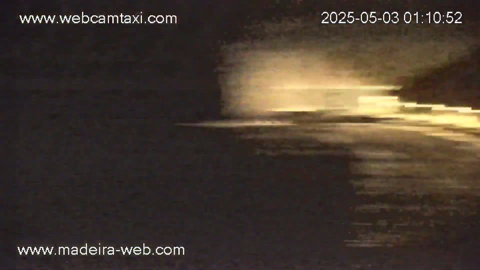 A blurry image shows a nighttime scene of light streaks on a dark body of water under a hazy sky.