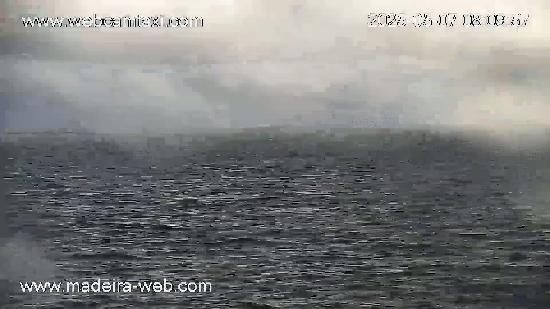 A hazy, overcast sky hangs over a dark, relatively calm body of water.