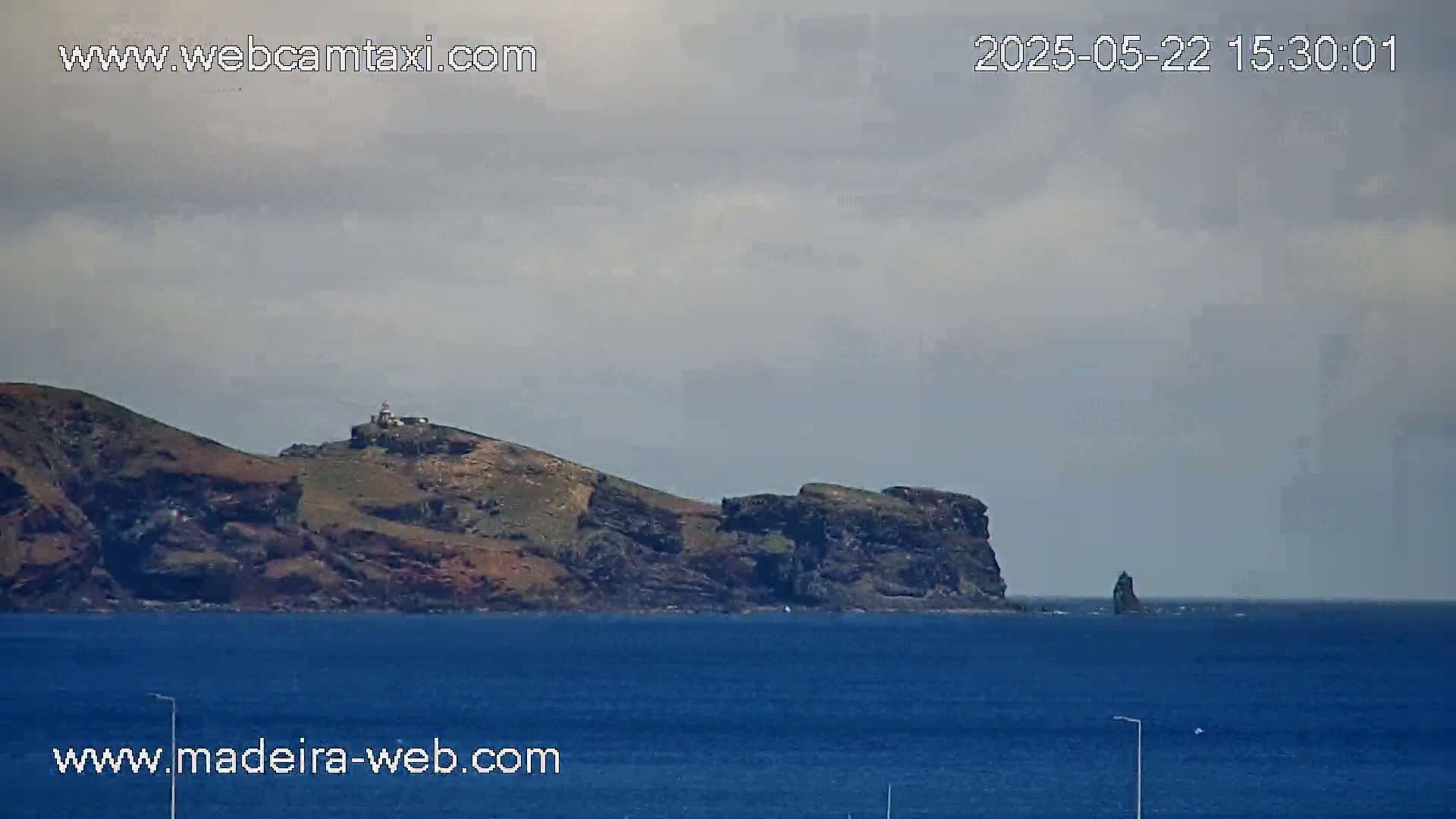 A rocky island with a lighthouse is visible across a calm, blue ocean under an overcast sky.