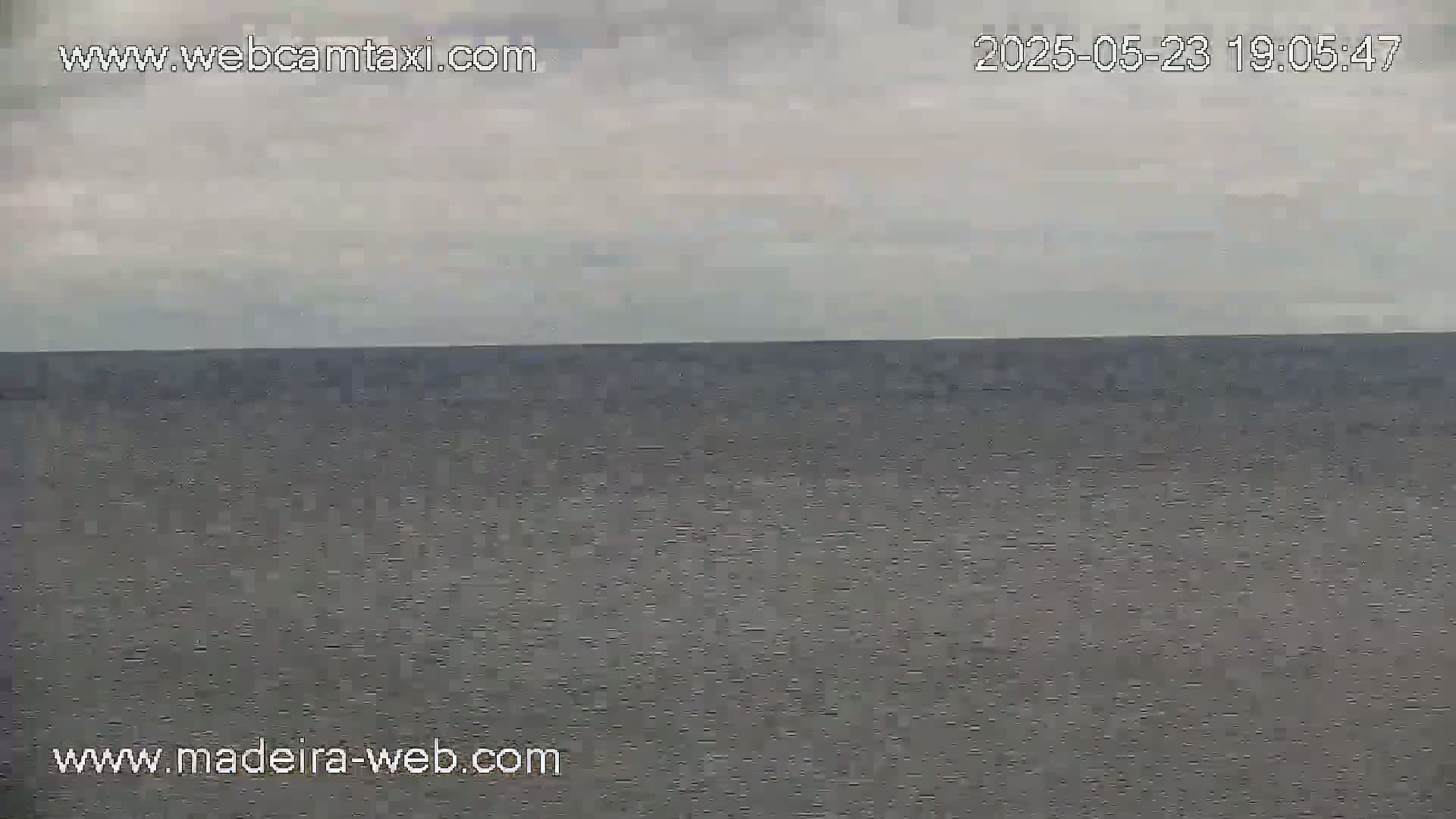 A mostly cloudy sky overlooks a calm, dark gray ocean.