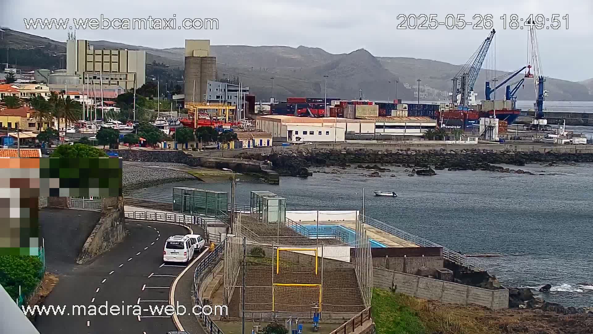 A coastal town with a harbor, cargo ships, and a small outdoor pool is seen on an overcast day.