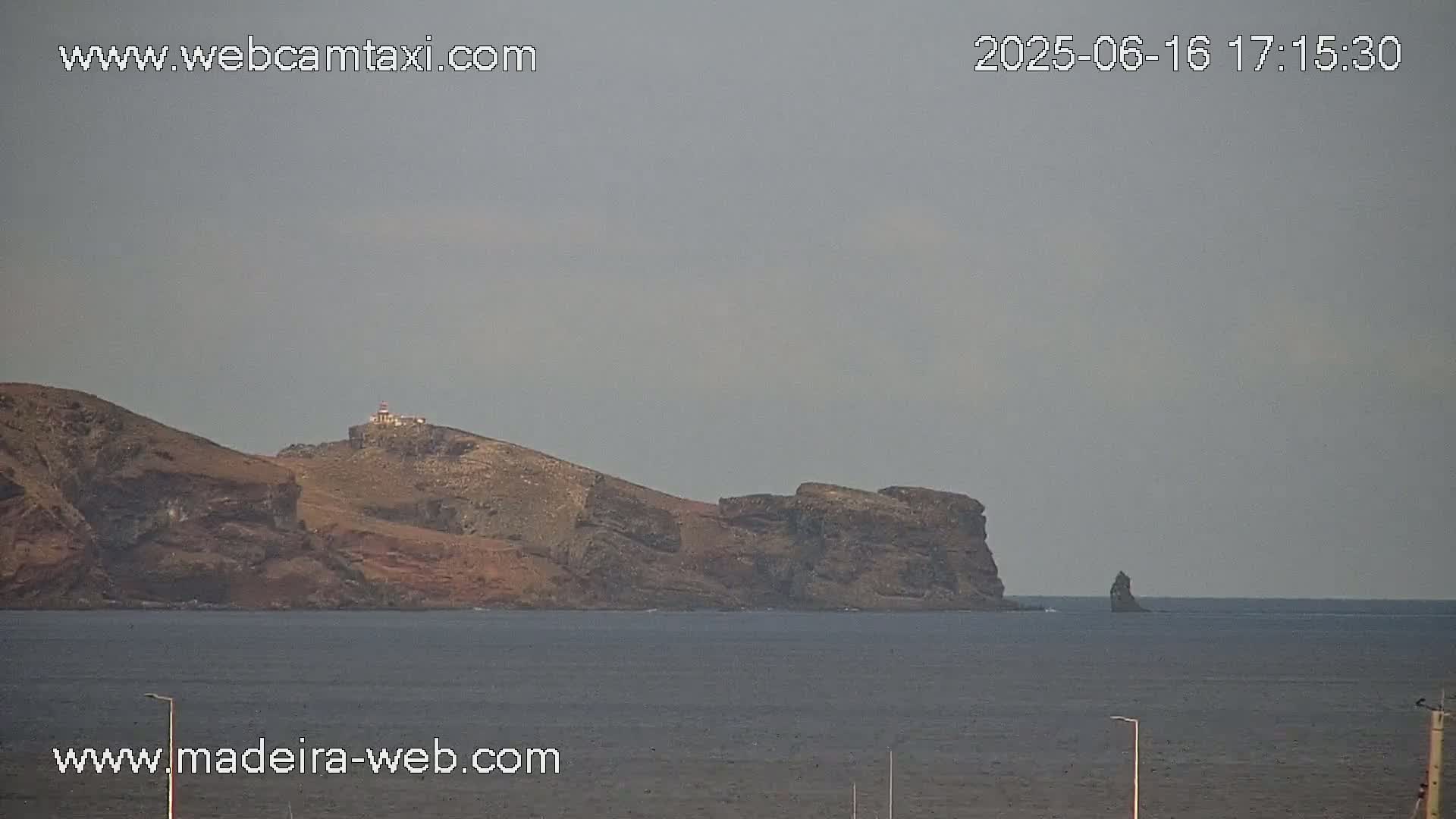 A rocky, mountainous island with a lighthouse is visible across a calm, gray body of water under an overcast sky.