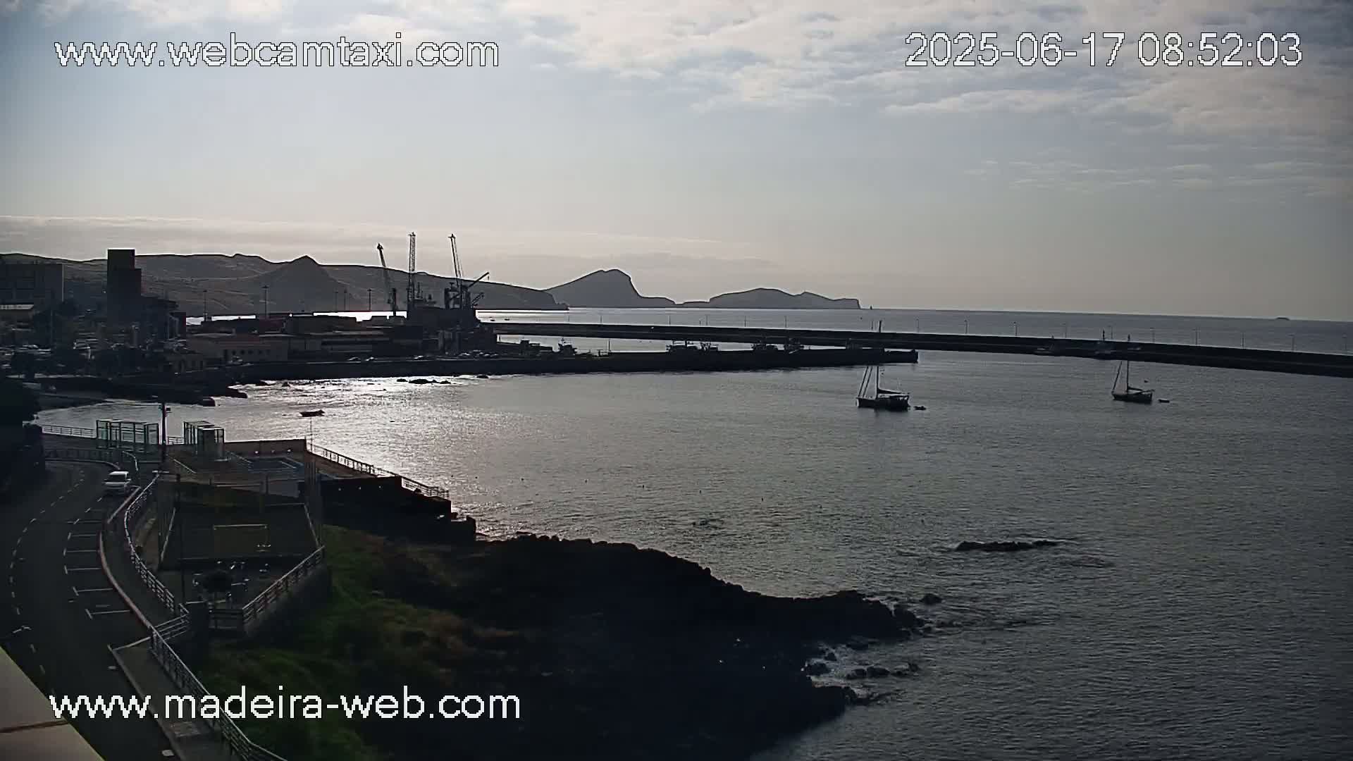 A harbor with several boats and a small town is visible under a cloudy sky.