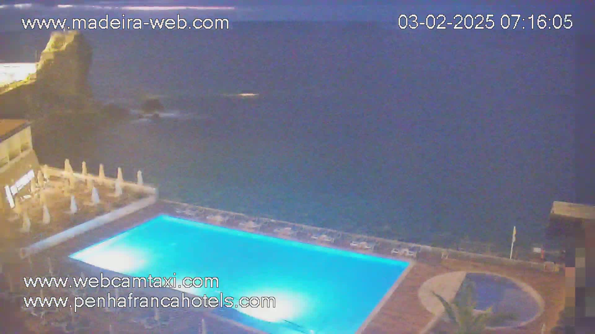 An illuminated swimming pool overlooks a dark ocean at night.