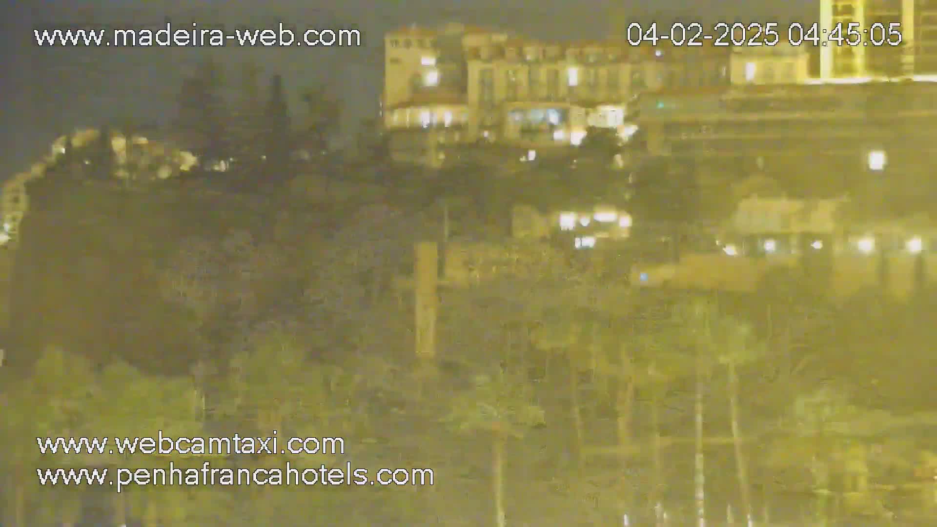 A nighttime long shot shows a hill covered in vegetation with a brightly lit hotel building perched atop it.
