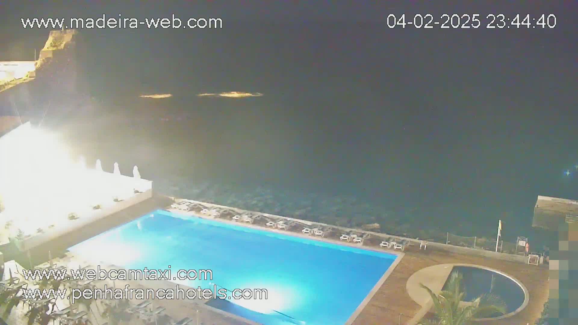 A nighttime view of a resort pool area next to the ocean under a dark sky.