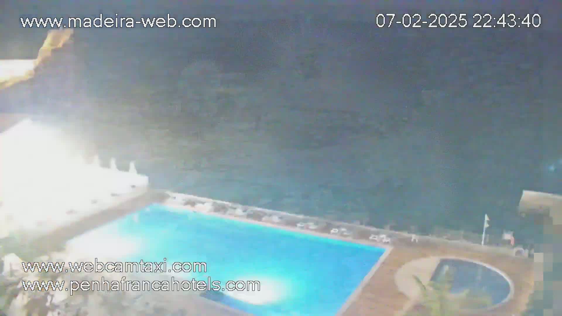 A nighttime aerial view shows a swimming pool at a resort overlooking a dark ocean.