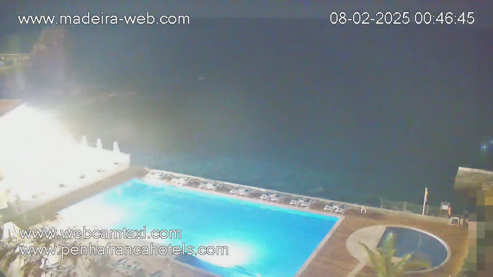 A nighttime view of an outdoor swimming pool and a smaller adjacent pool, overlooking a dark ocean under a clear sky.