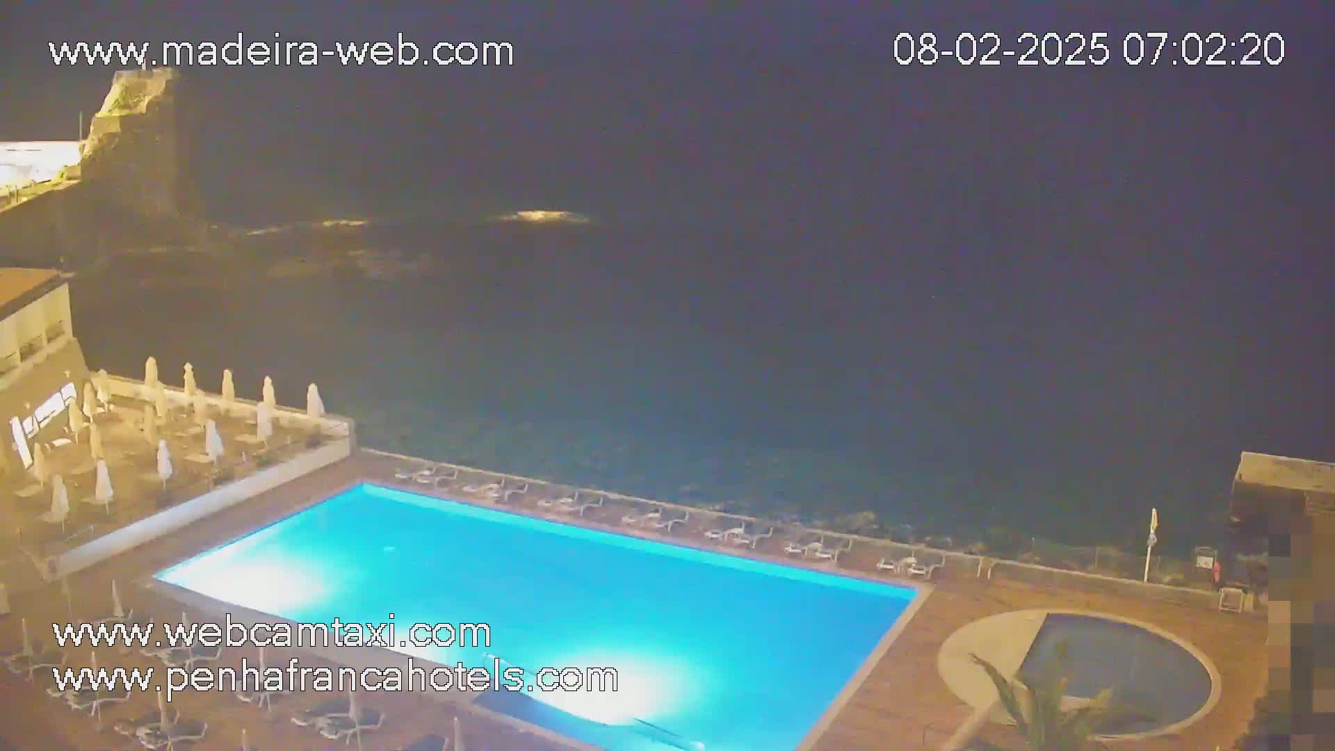 A nighttime view of a rectangular swimming pool at a hotel overlooking a dark ocean.