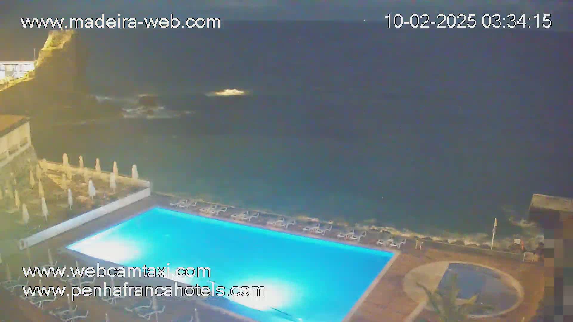 A nighttime view of a resort pool area next to a dark ocean with small waves.