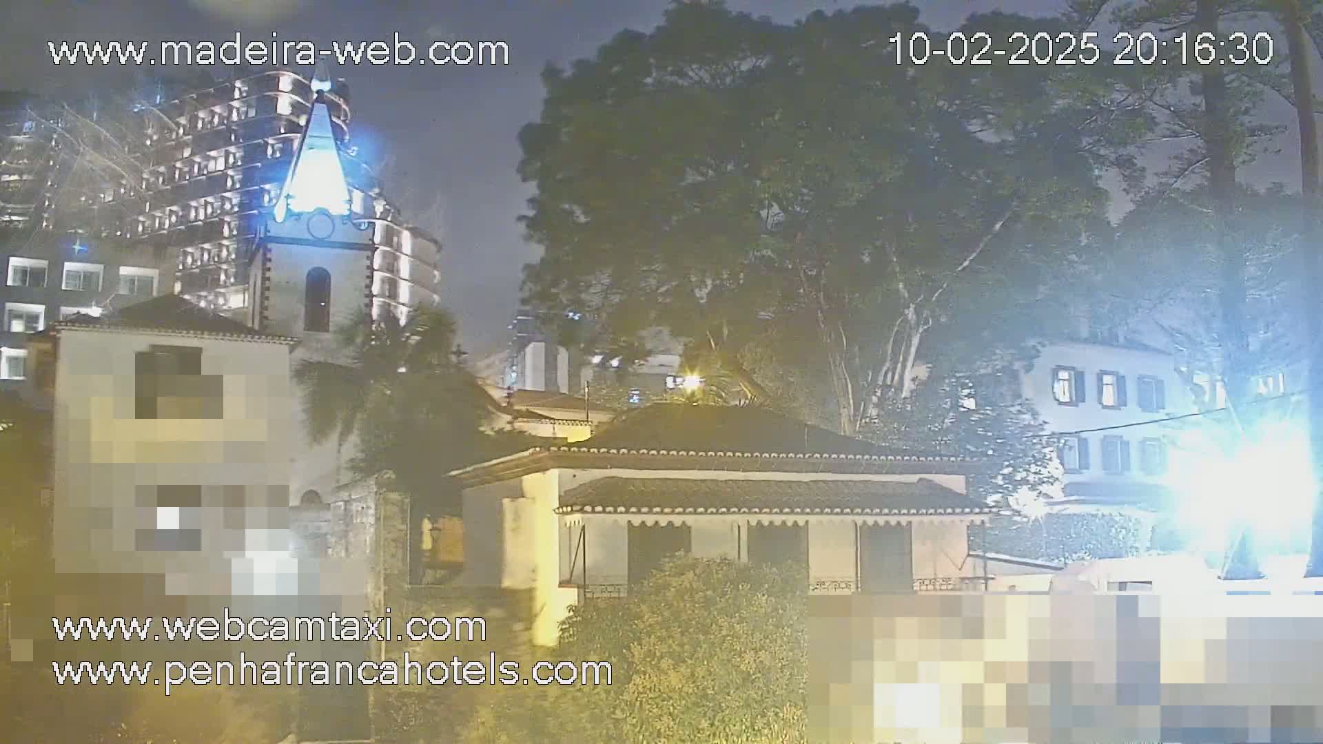A nighttime view of buildings, including a church steeple, partially obscured by trees under a hazy sky.