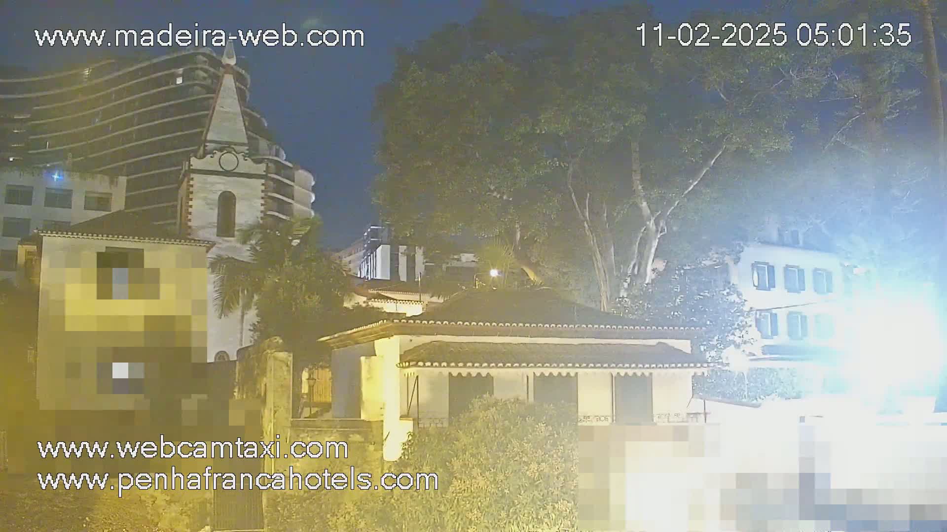 A nighttime view of several buildings, including a church and a low building with shrubbery, under a partly cloudy sky.