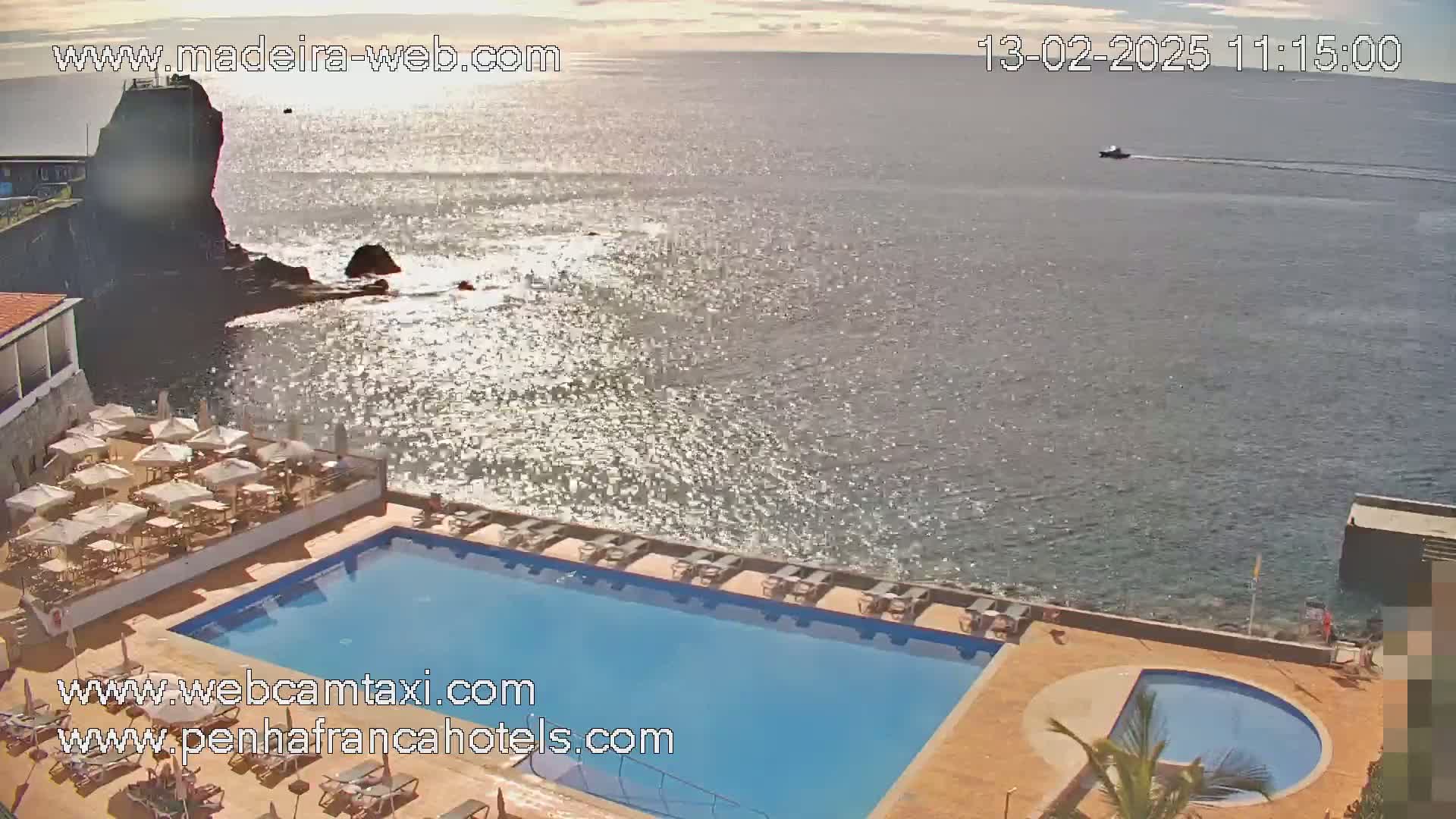 A sunny day overlooking a sparkling ocean from a resort with a large rectangular pool and a smaller circular pool, with lounge chairs surrounding them.