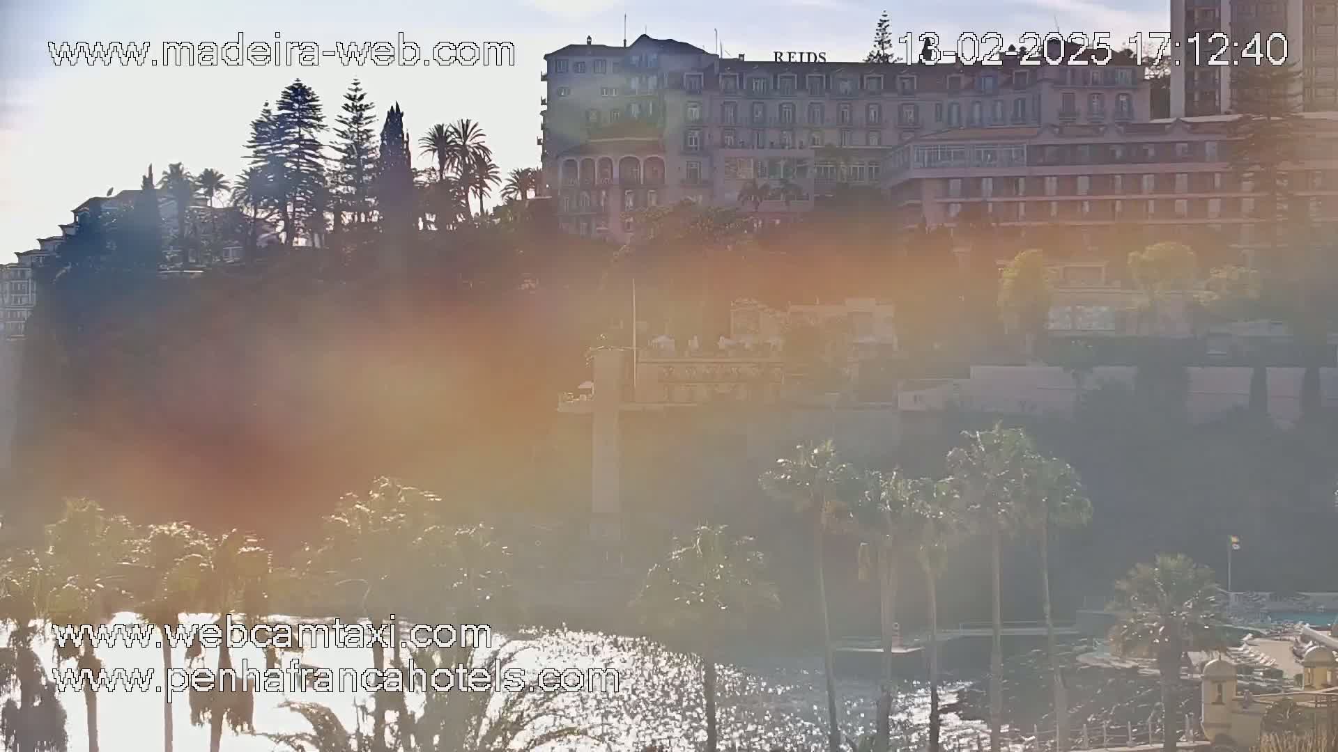 A hazy, sunny day reveals a hillside with palm trees and a large hotel building overlooking a body of water.