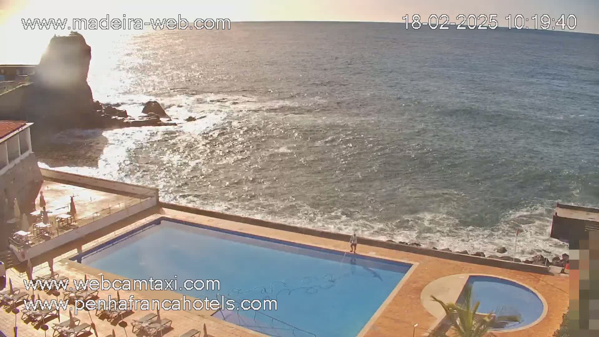 An outdoor swimming pool and smaller circular pool sit adjacent to a rocky coastline with a somewhat choppy ocean under a mostly sunny sky.