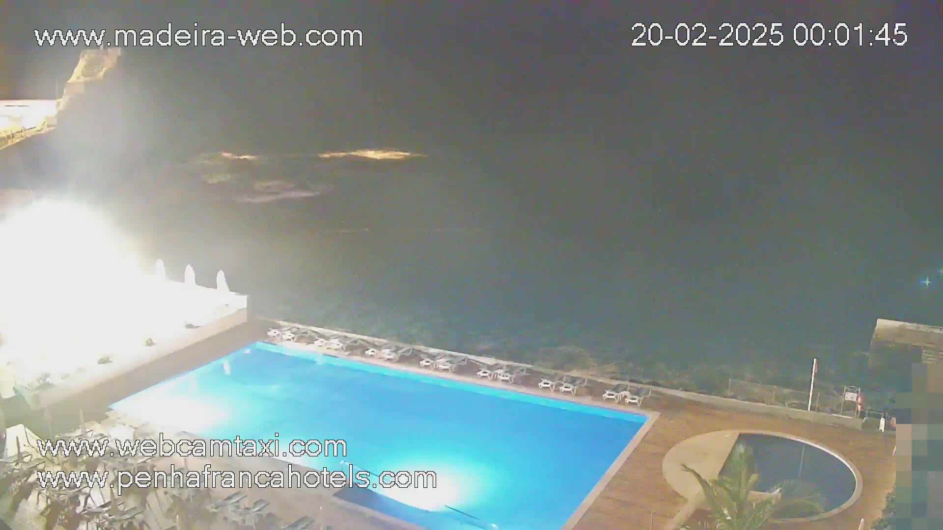 A nighttime view of an outdoor swimming pool adjacent to a dark ocean under a clear sky.