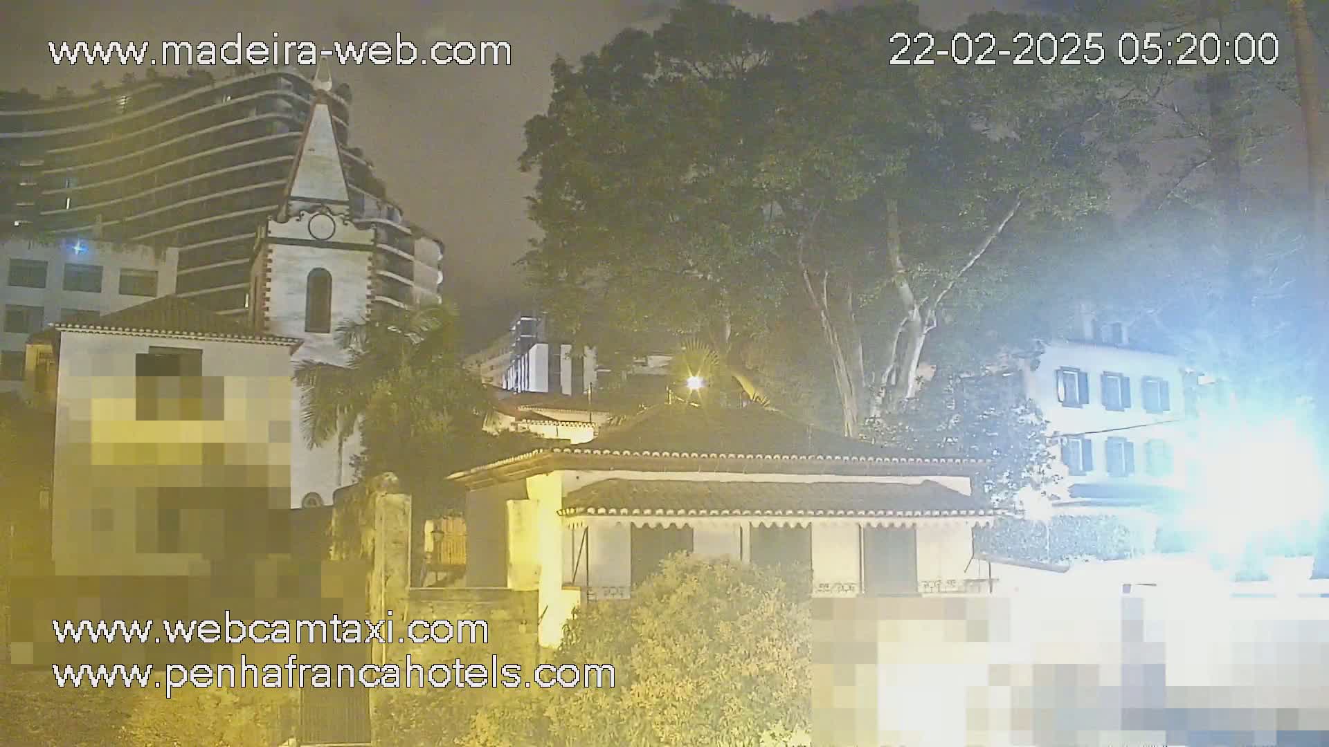 Nighttime view of buildings, including a church and a multi-story structure, partially obscured by trees under hazy or foggy conditions.