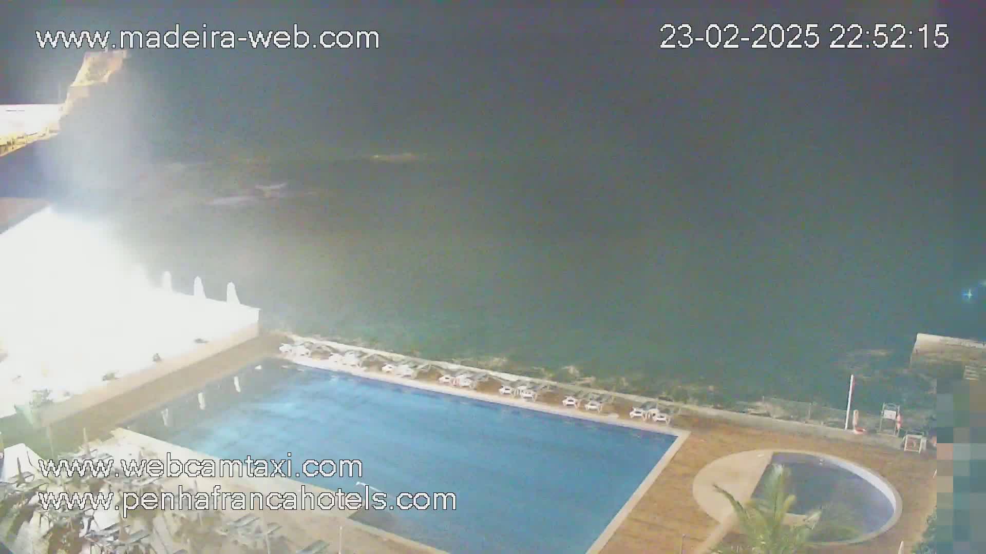 An outdoor nighttime scene shows a swimming pool next to the ocean under a cloudy sky.