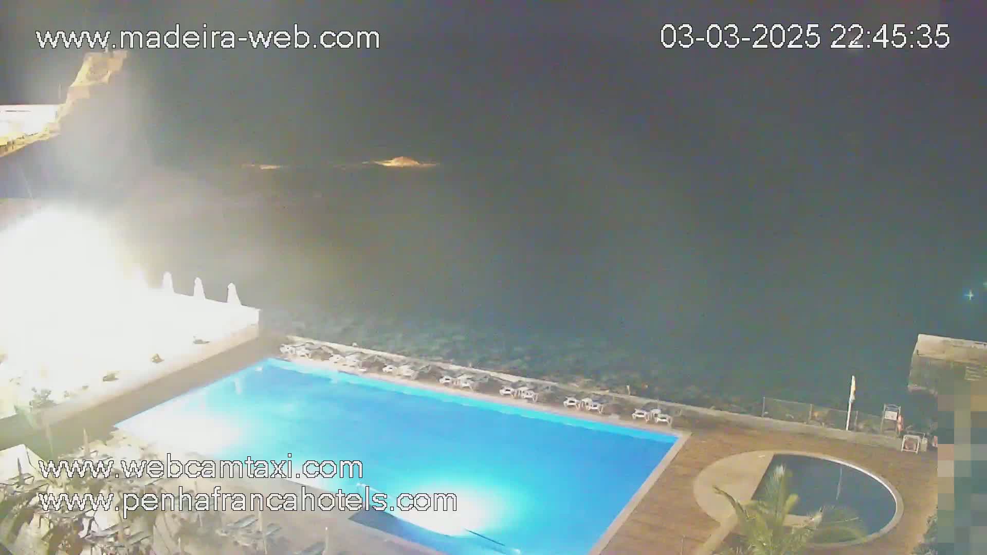 A nighttime view of an outdoor swimming pool at a resort overlooking a dark ocean.